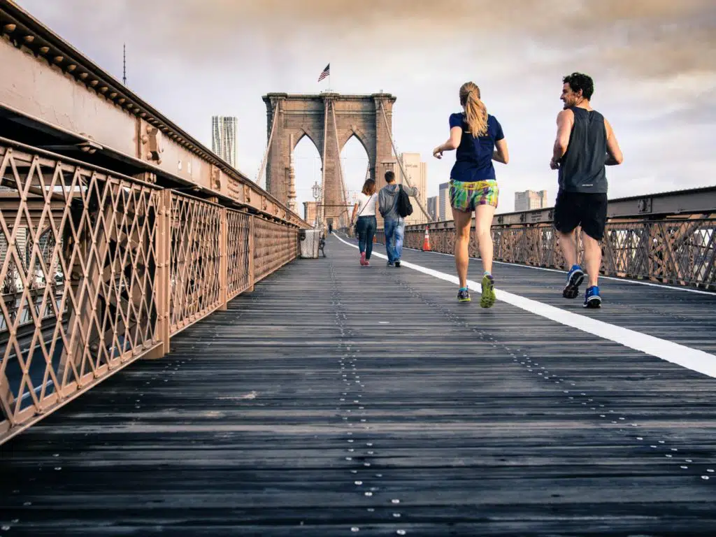 man and woman in black tops jogging at bridge under clear skies