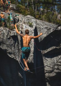 Slackline suspendend from rock face while a shirtless man balances on it